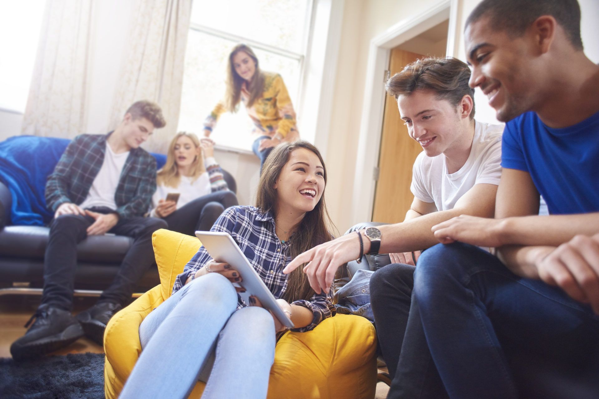 College students and roommates hanging out together in a student apartment, streaming and studying with laptops and tablets during back-to-school move-in.
